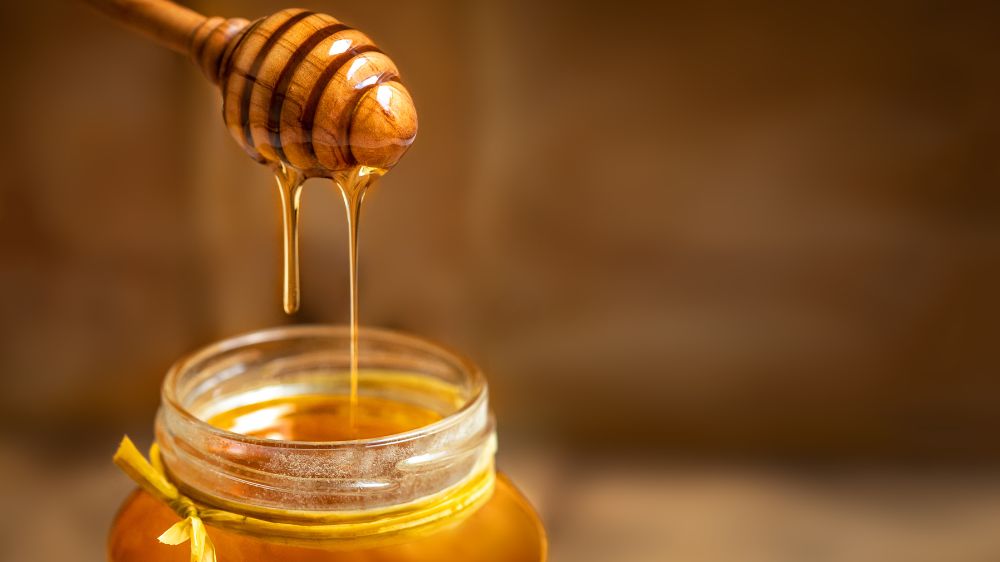 طرف پر از عسل و قاشق پر از عسل در بالای آن
