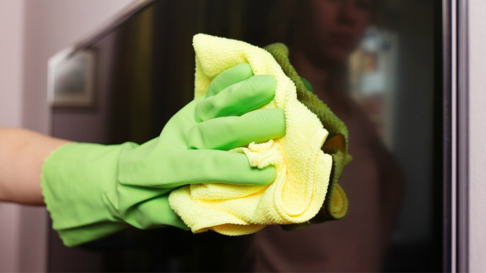 تمیز کردن صفحه نمایش تلویزیون با دستمالی زرد و دستکش سبز