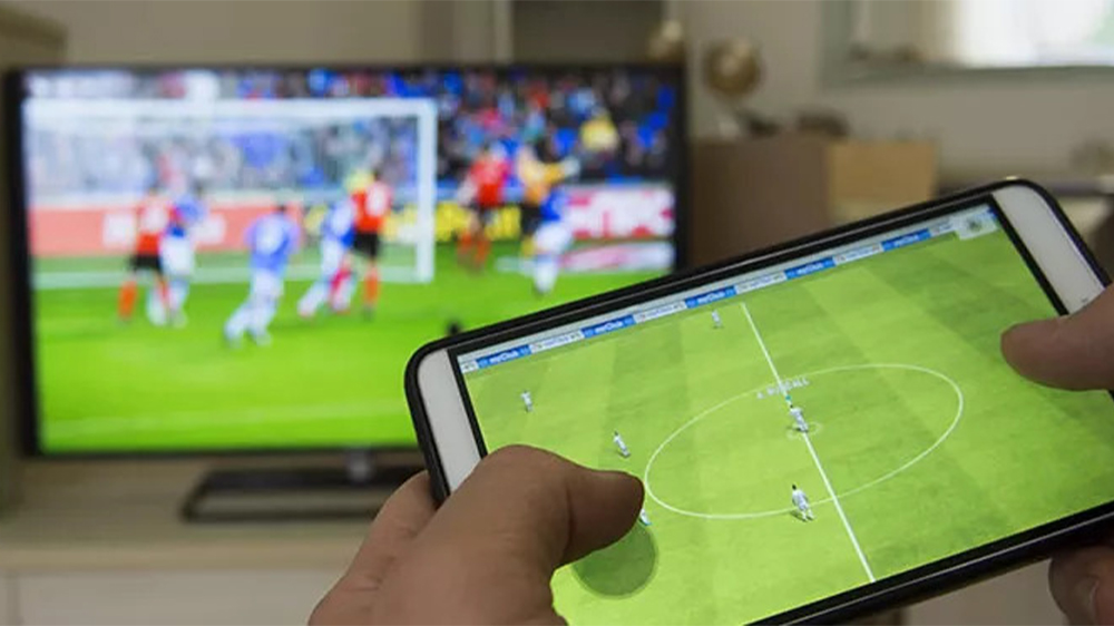 یک گوشی متصل‌شده به تلویزیون و فردی که در حال بازی فوتبال است