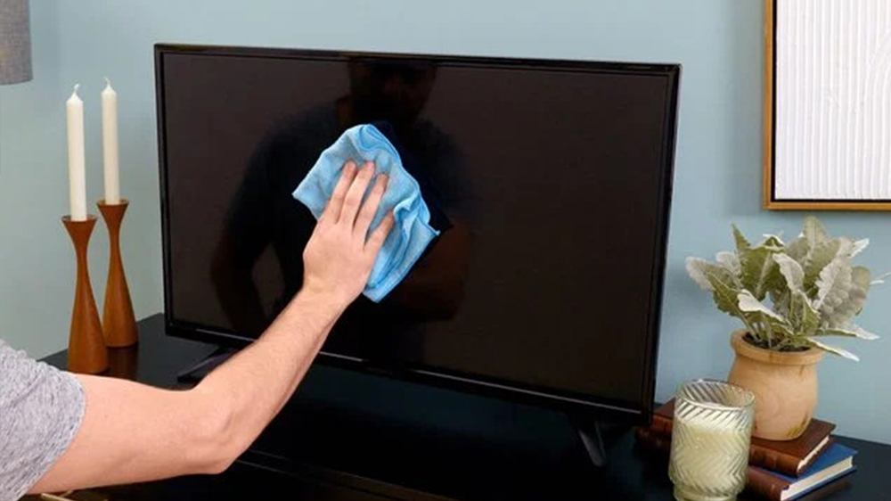مردی در حال تمیز کردن تلویزیون کنار شمعدان و گلدان با دستمال آبی