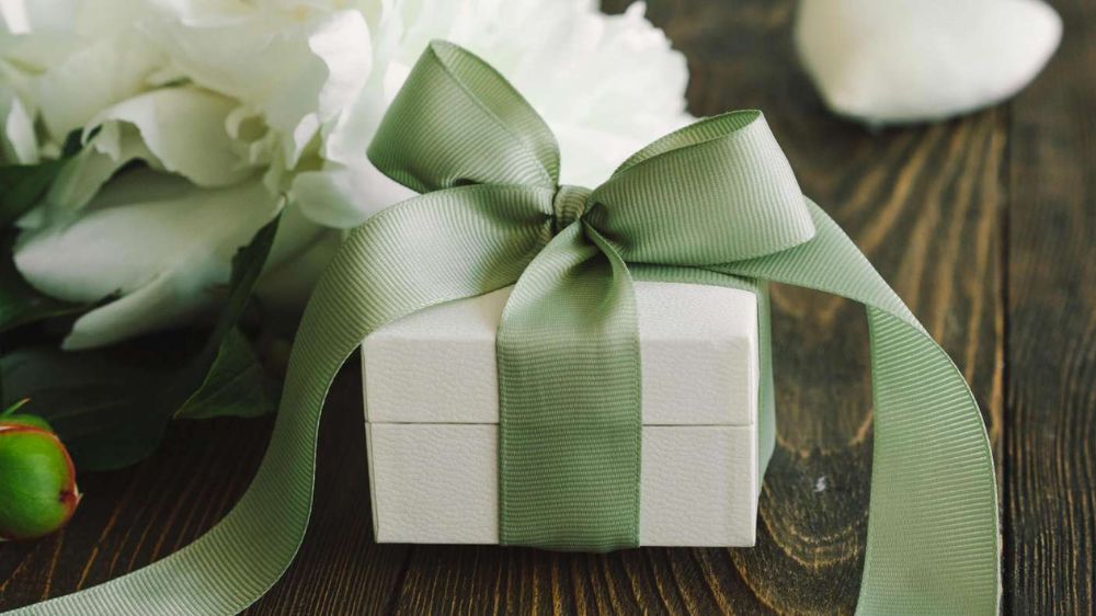 یک جعبه هدیه کوچک سفید رنگ با روبان سبز روی یک میز چوبی