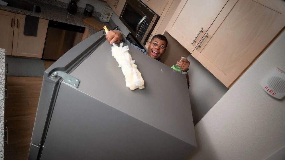 مرد سیاه‌پوستی در حال تمیز کردن بالای یخچال