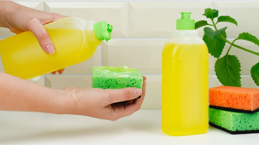 فردی در حال ریختن مایع ظرفشویی زرد رنگ روی اسفنج
