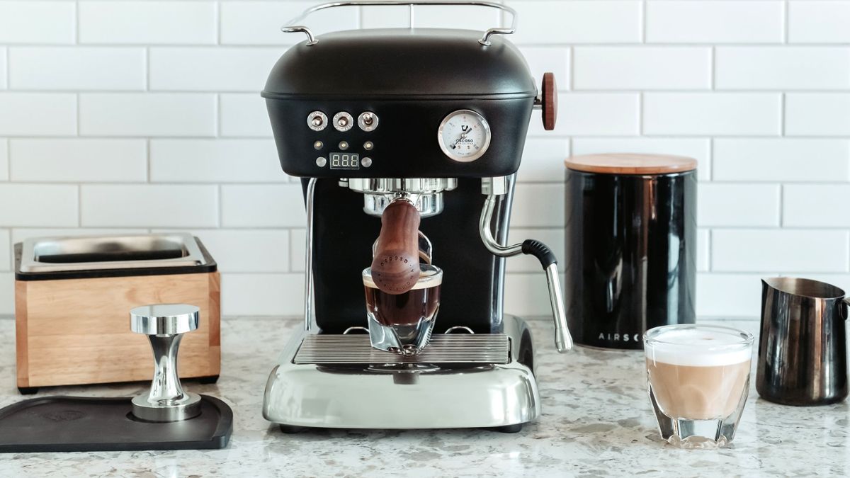 یک دستگاه اسپرسو ساز خانگی در کنار لیوان قهوه روی کانتر آشپزخانه