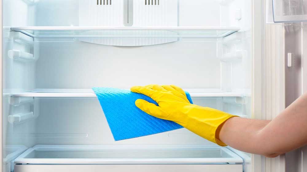 فردی در حال تمیز کردن فضای درونی یخچال با دستمال آبی