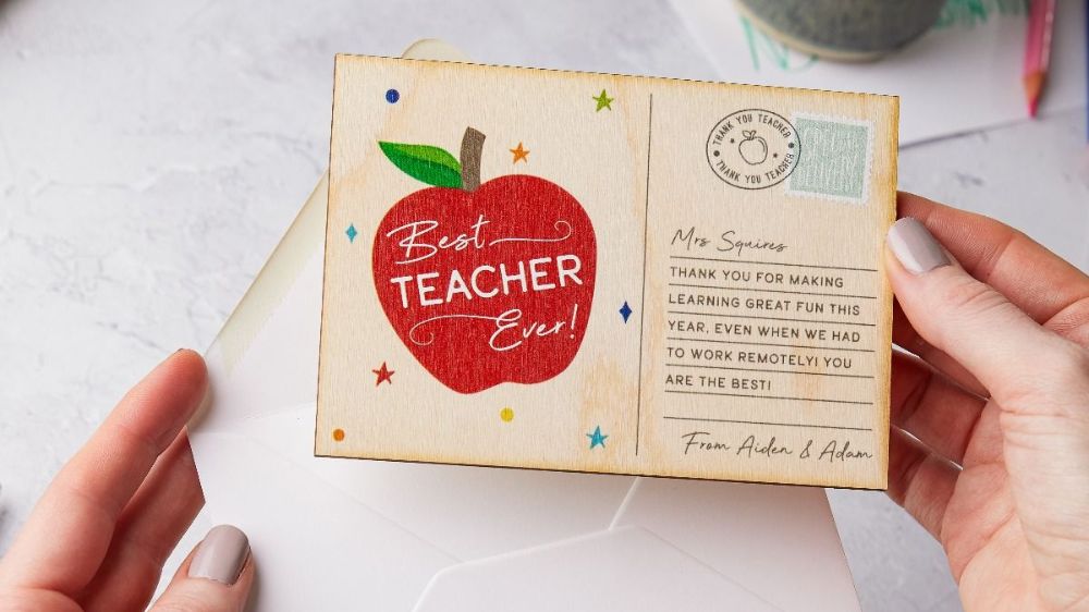 دستان یک نفر در حال گذاشتن کارت پستال طرح سیب برای روز معلم در پاکت نامه سفید