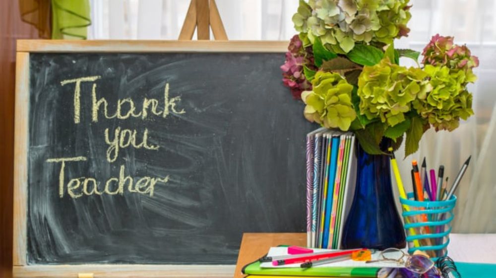پیام تشکر از معلم روی یک تخته سیاه که کنار آن یک گلدان قرار دارد