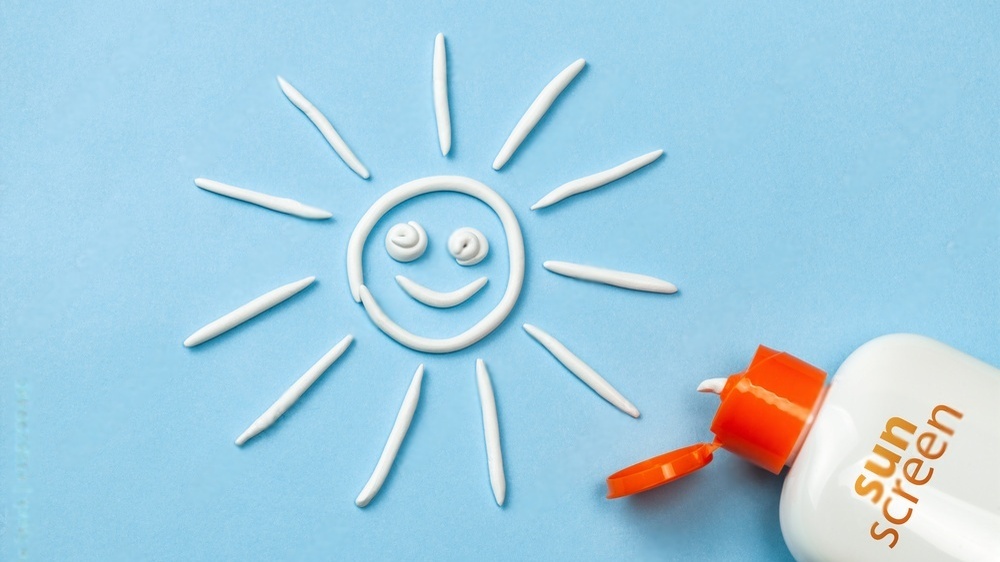 یک کرم ضدآفتاب با درب نارنجی در گوشه تصویر با یک شکلک خورشید خندان ترسیم‌شده با ضدآفتاب در یک پس‌زمینه آبی رنگ
