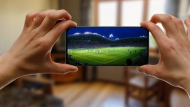 تصویر یک گوشی هوشمند در دستان یک مرد در حال پخش یک مسابقه فوتبال