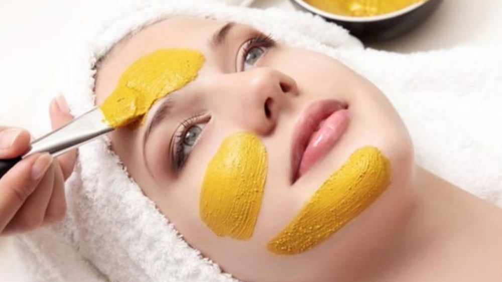 زنی که خوابیده و فرد دیگری دارد روی صورت او ماسک زرد رنگ می‌زند