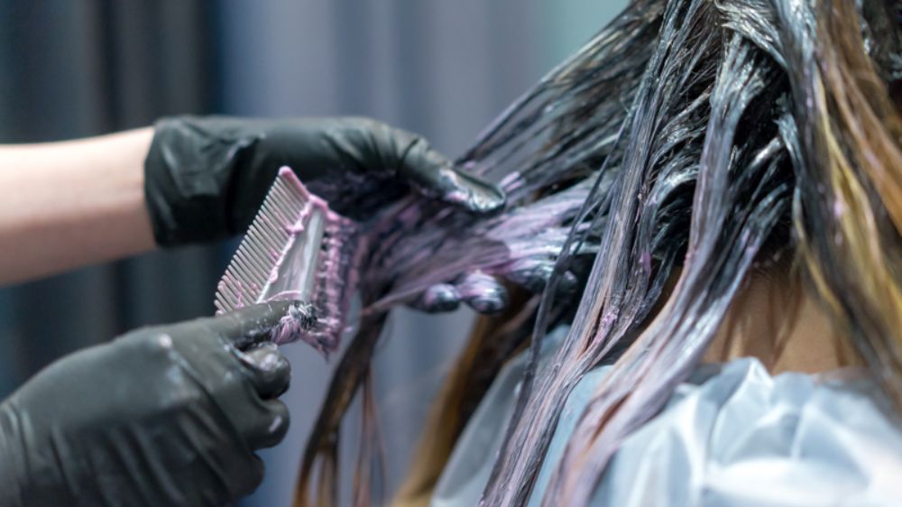 آرایشگر در حال رنگ کردن موهای یک خانم از نمای کلوزاپ