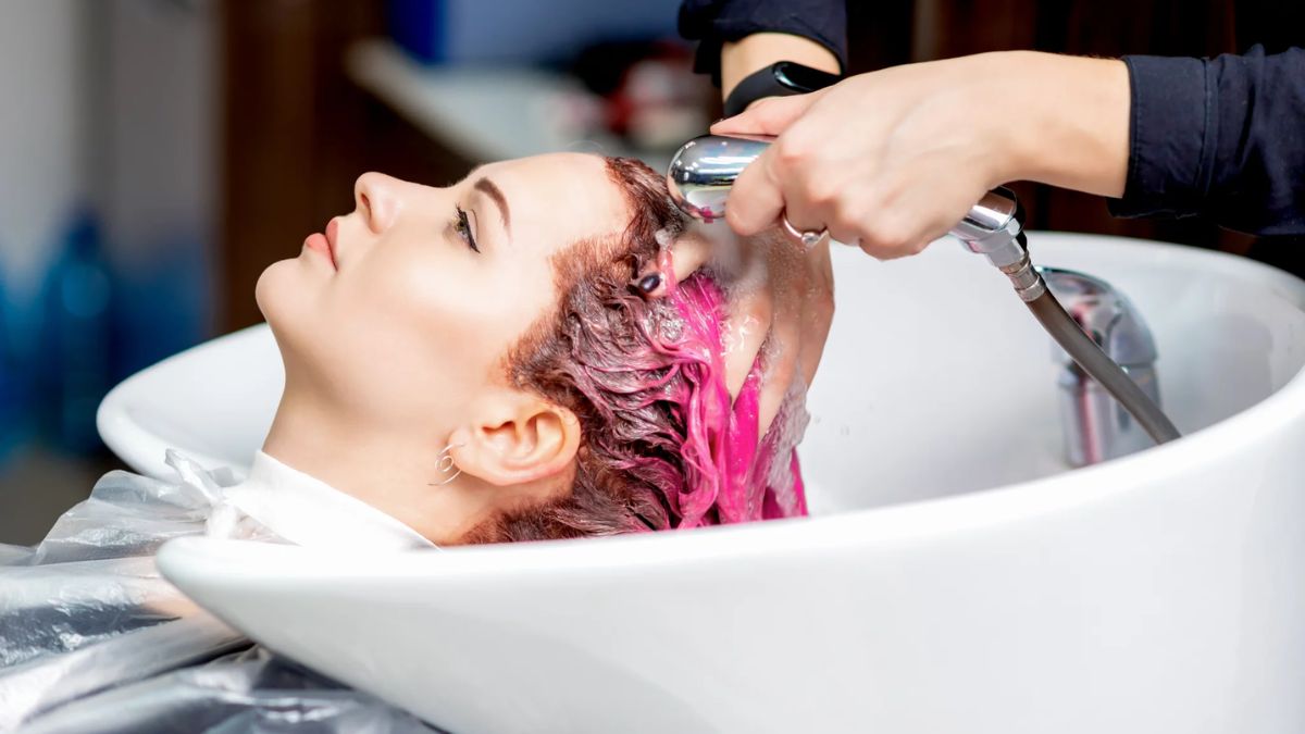 آرایشگر در حال شستن موهای رنگ شده یک خانم در آرایشگاه
