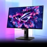 مانیتور گیمینگ با لوگوی ASUS ROG در مرکز صفحه، روی پایه‌ای محکم و در پس‌زمینه‌ای با نورهای بنفش و آبی