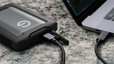 هارد اکسترنال سندیسک Professional G Drive ArmorATD به رنگ مشکی و لوگوی G که با یک کابل USB به لپ‌تاپی روی سطح سنگی متصل شده است