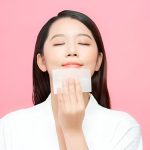 یک زن زیبای کره‌ای که چشمانش را بسته است و با یک دستمال در حال پاک کردن صورتش است