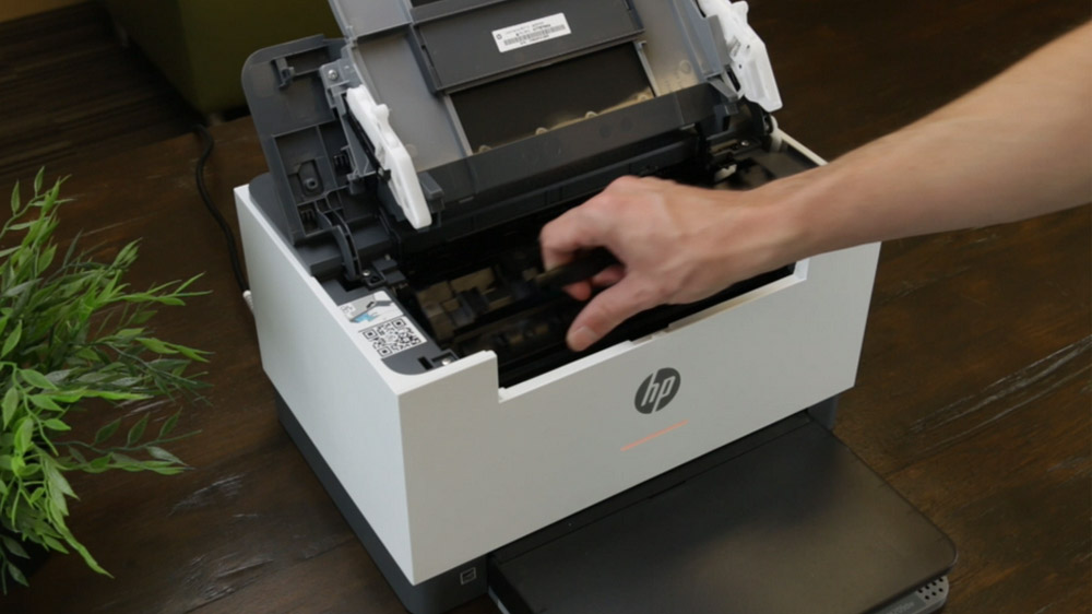 شخصی در حال خارج کردن کارتریج یک پرینتر HP روی میز چوبیشخصی در حال خارج کردن کارتریج یک پرینتر HP روی میز چوبی