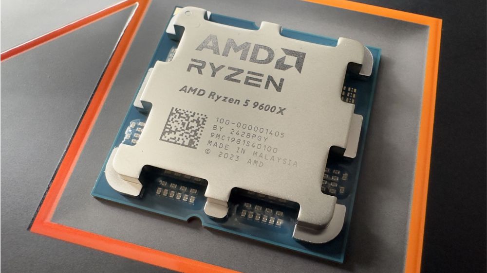 پردازنده ایامدی Ryzen 5 9600X با لوگو AMD Ryzen در بالا که روی سطح خاکستری و نارنجی قرار گرفته
