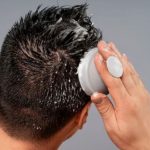 نمای پشت سر مردی که در حال استفاده از اسکراب سر است.