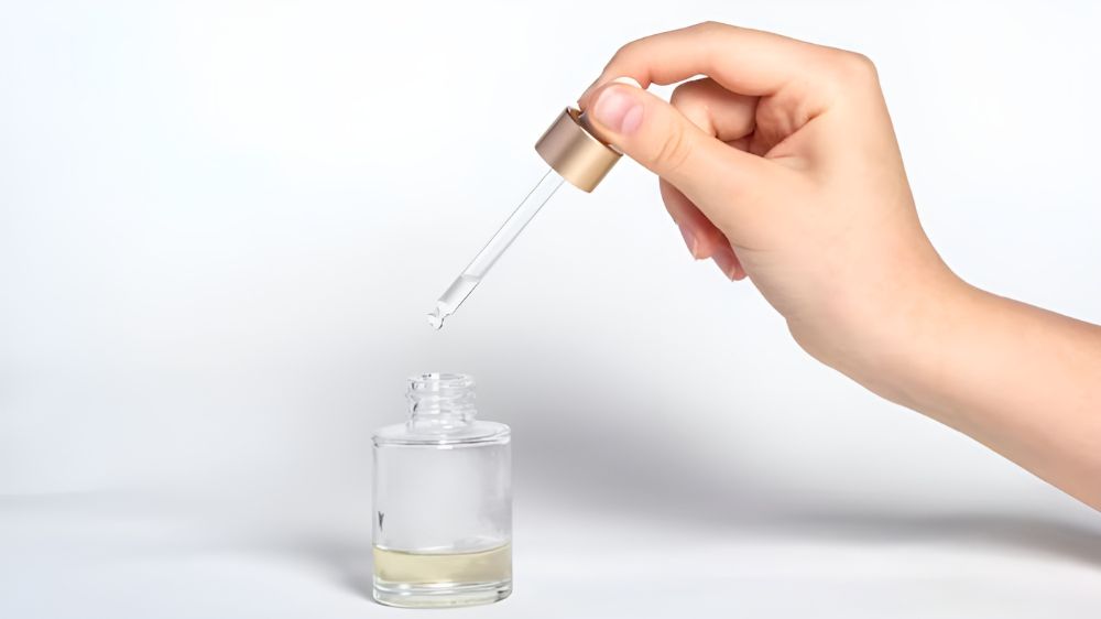 نمای نزدیک از دستی که با قطرهچکان در حال برداشتن اسنس از ظرف است.