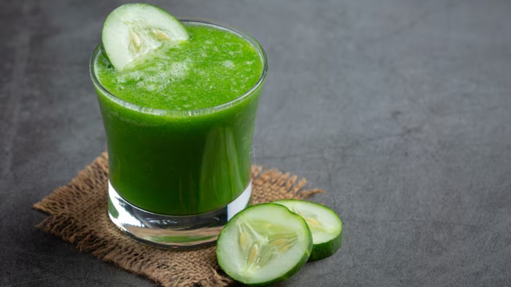 یک لیوان آب خیار در کنار چند حلقه خیار تازه چیده شده است.