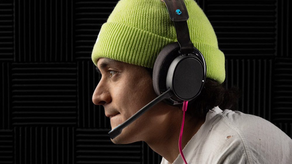 هدست Skullcandy SLYR Pro روی گوش گیمر در پسزمینه دیوار مشکی آکوستیک