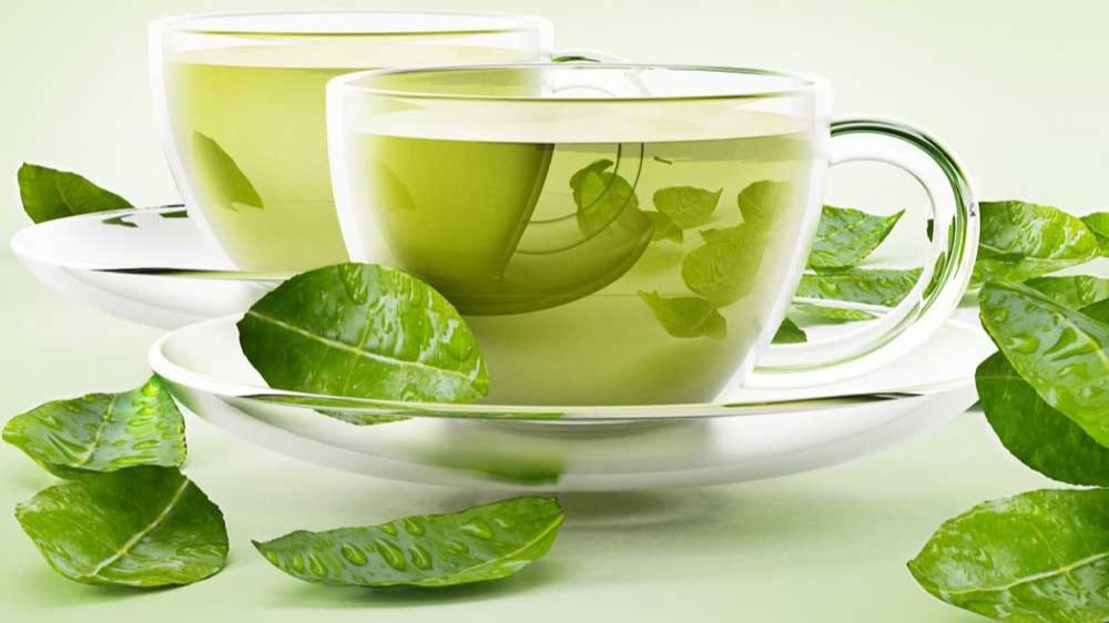 برگ های چای سبز و دو استکان چای سبز در کنار هم قرار دارند و پس زمینه نیز سفید است