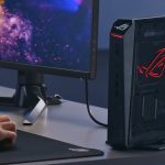 یک نفر در حال کار کردن با مینی کامپیوتر گیمینگ asus rog سری nuc متصل به مانیتور rog با ماوس و کیبورد روی یک میز مرتب