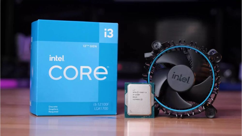 پردازنده اینتل مدل core i3-12100f در وسط به همراه جعبه آبی رنگش در سمت چپ و فن و هیتسینک در سمت راست، به حالت ایستاده روی میز قهوهای رنگ با پسزمینه مات