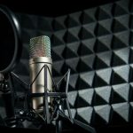 میکروفن استودیویی نقره‌ای رنگ در شوک‌ماونت به همراه پاپ فیلتر، در محیطی با پوشش فوم آکوستیک
