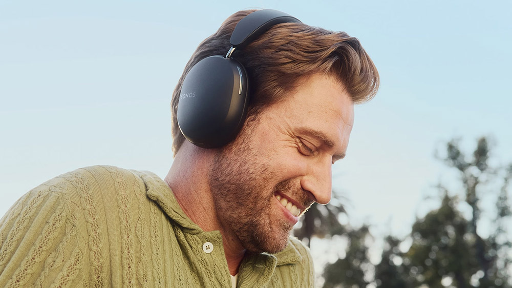 هدفون دور گوشی Sonos Ace روی گوش یک مرد خندان با درخت در پسزمینه
