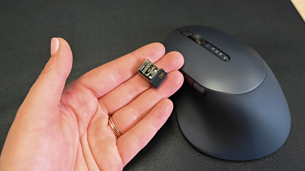 یک دانگل USB در دست یک نفر در کنار موس بی سیم MS900 دل
