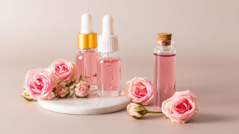 چند بطری گلاب و چند گل رز در یک پس‌زمینه صورتی