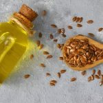 یک شیشه روغن کتان در کنار یک قاشق چوبی پر از دانه کتان