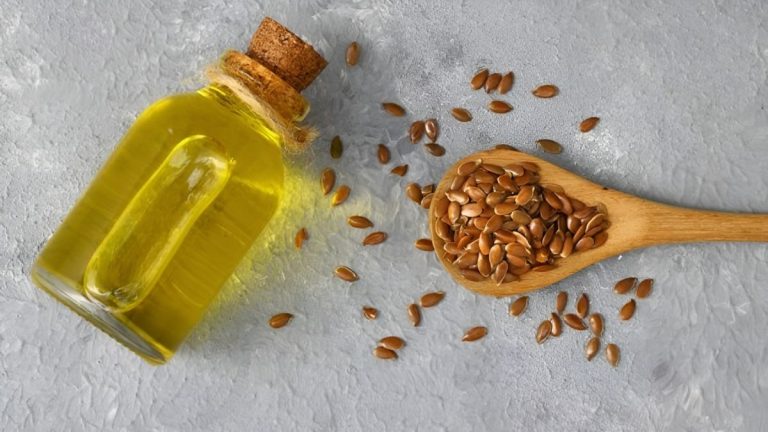 یک شیشه روغن کتان در کنار یک قاشق چوبی پر از دانه کتان