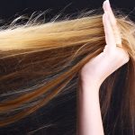 خانمی با موهای بور خود را در دست گرفته است با پس زمینه تیره