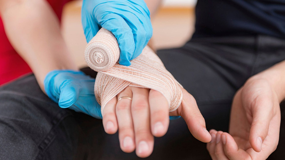 کادر درمان با دستکش پزشکی آبی در حال بستن باند دور دست یک نفر