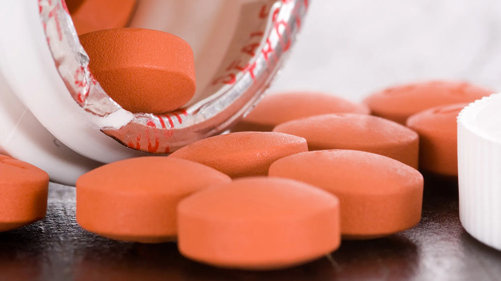 قرص های ایبوپروفن در حال بیرون ریختن از قوطی سفید روی سطح چوبی تیره