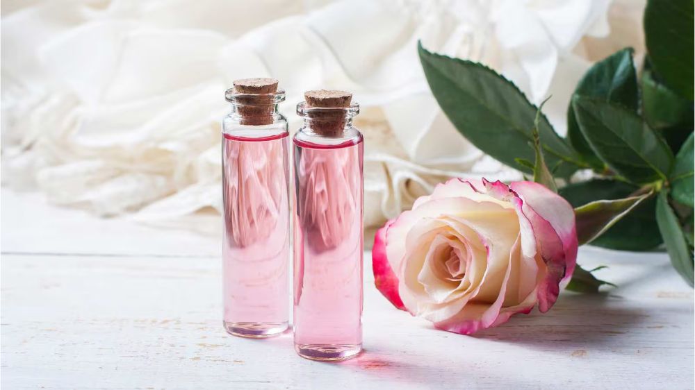 دو بطری گلاب کنار یک رز صورتی