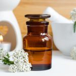 روغن بومادران داخل بطری در کنار چند شاخه گل بومادران