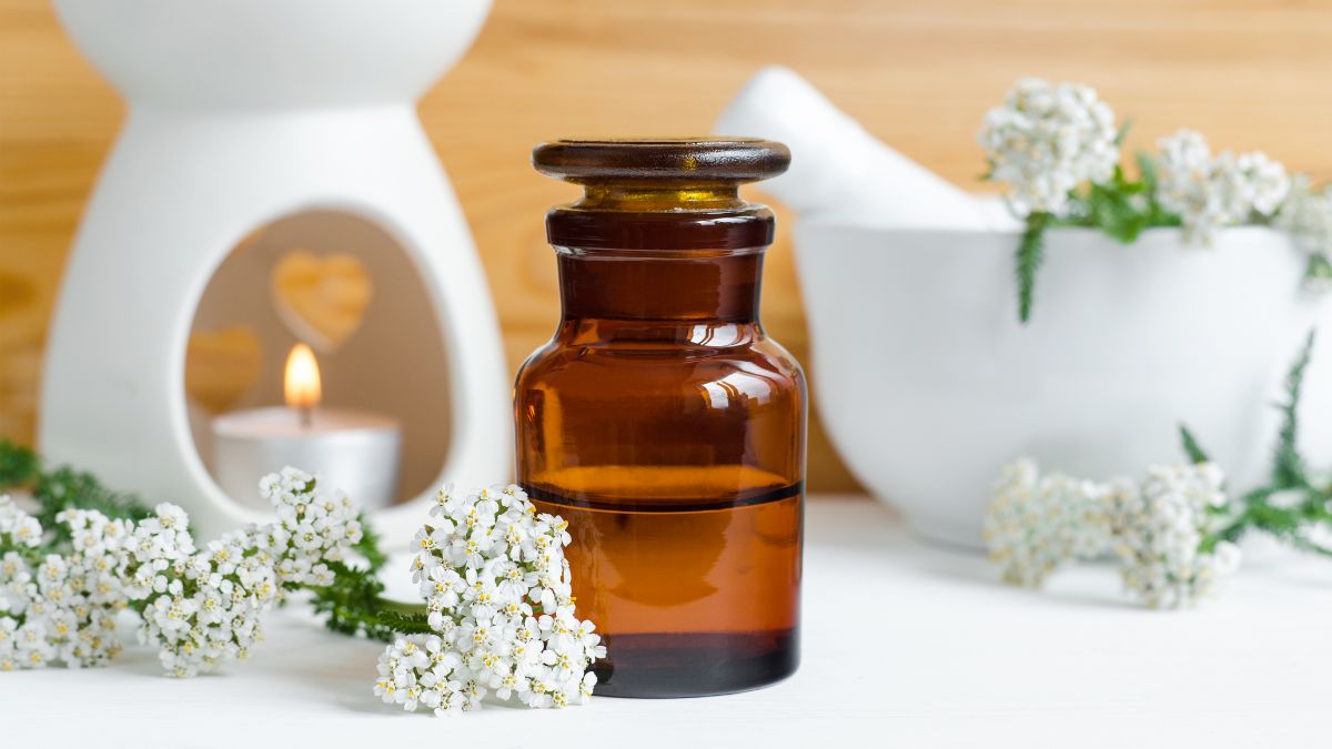روغن بومادران داخل بطری در کنار چند شاخه گل بومادران