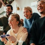 چهار دوست در حال بازی با کنسول، با هیجان و شادی فریاد می‌زنند