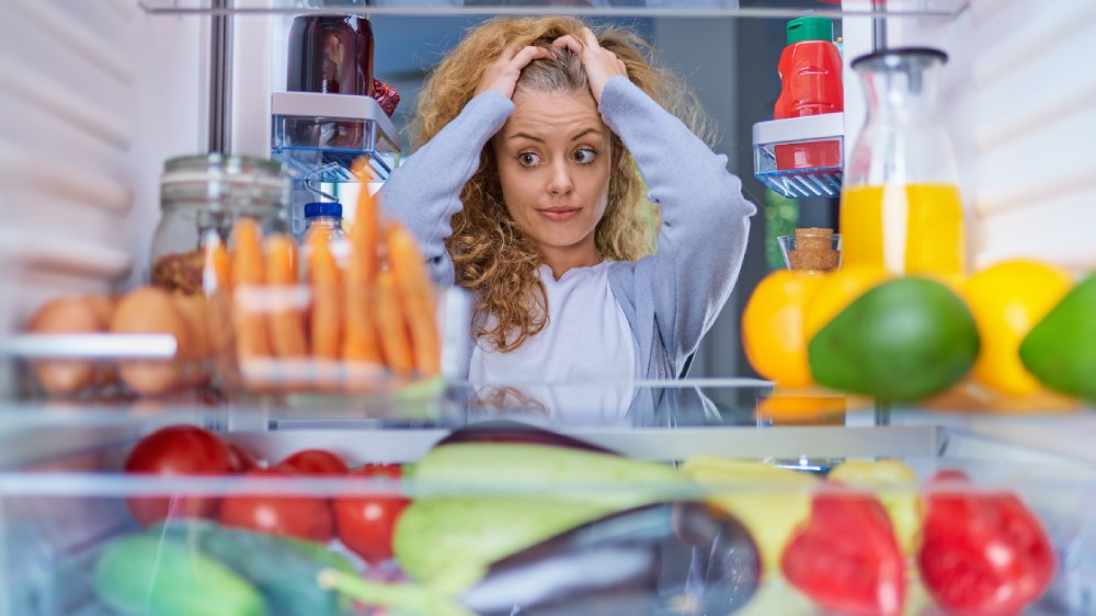 زنی کلافه و سردرگم از داخل به یخچالی شلوغ و نامرتب نگاه می‌کند و نمی‌داند چه کند