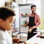 پدر و پسر خندان در حال آشپزی کردن در حالی که درب یخچال باز است