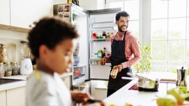 پدر و پسر خندان در حال آشپزی کردن در حالی که درب یخچال باز است