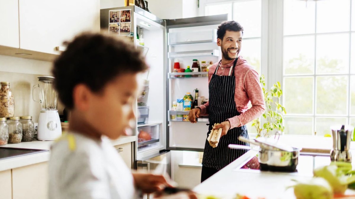 پدر و پسر خندان در حال آشپزی کردن در حالی که درب یخچال باز است