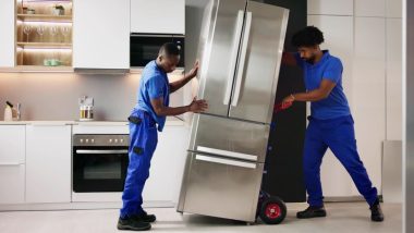 دو مرد در حال جابجایی یک یخچال استیل بزرگ در یک آشپزخانه با طراحی مدرن