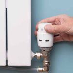 یک دست در حال تنظیم کردن شیر ترموستات رادیاتور با پس زمینه یک دیوار آبی