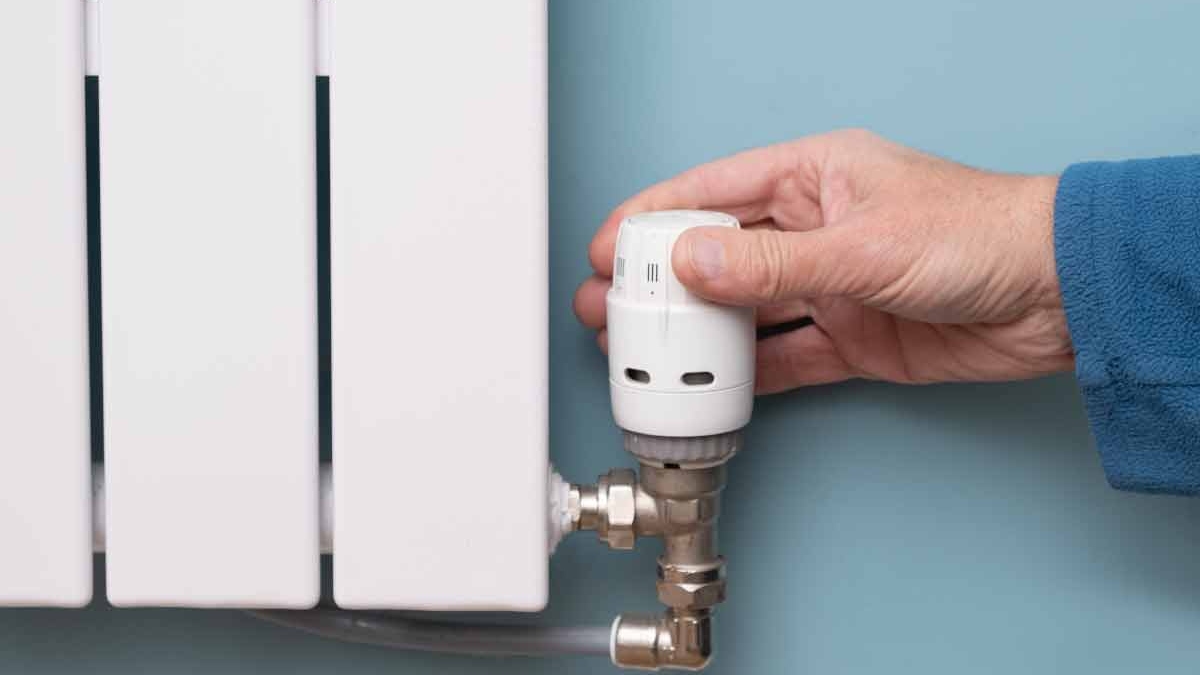 یک دست در حال تنظیم کردن شیر ترموستات رادیاتور با پس زمینه یک دیوار آبی