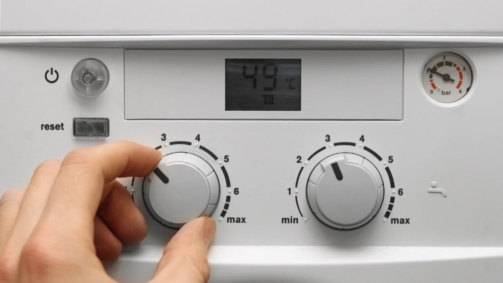 دست یک نفر در حال تنظیم کردن دمای آب یک پکیج دیواری