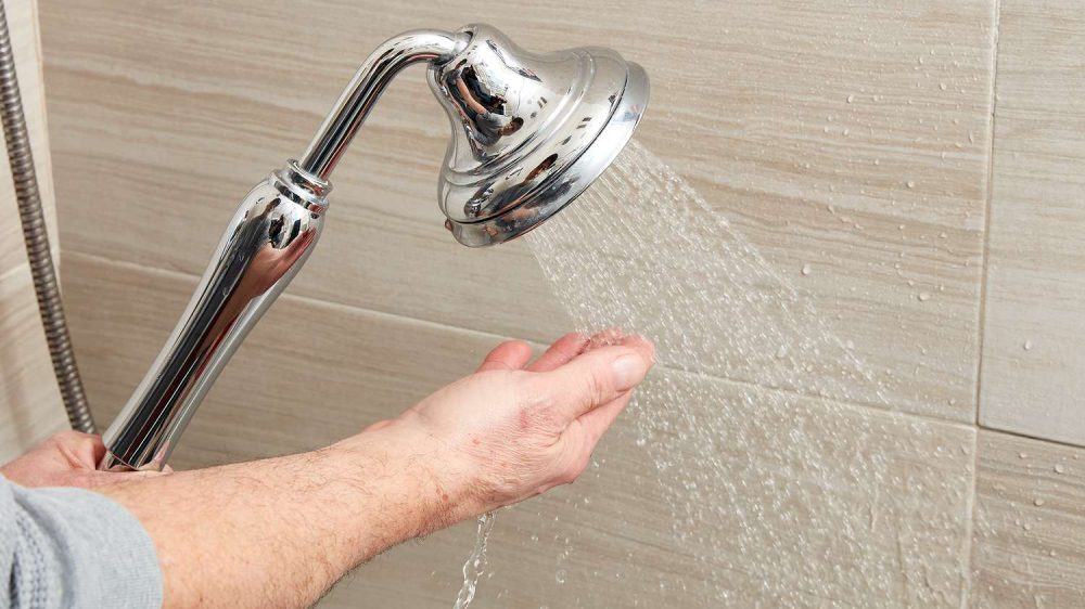 دست یک نفر در حال تست کردن دمای آب جاری از دوش حمام
